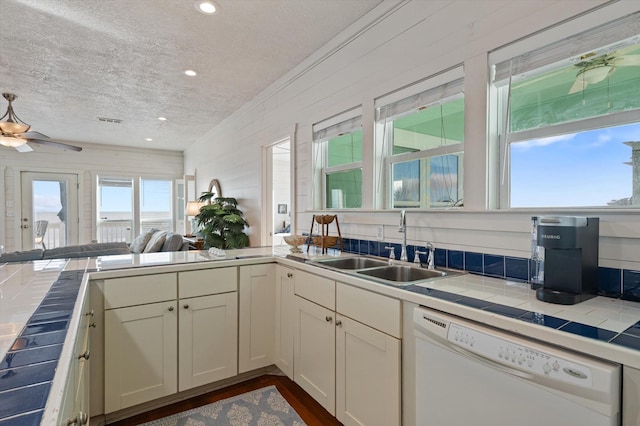 kitchen with dishwasher, white cabinets, sink, a textured ceiling, and tile counters