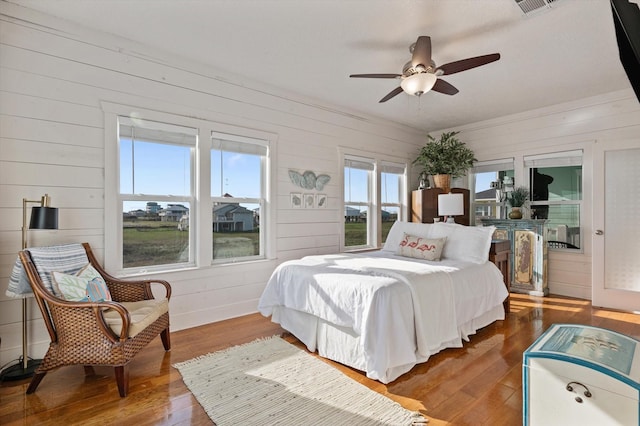 bedroom featuring multiple windows, ceiling fan, hardwood / wood-style floors, and wood walls