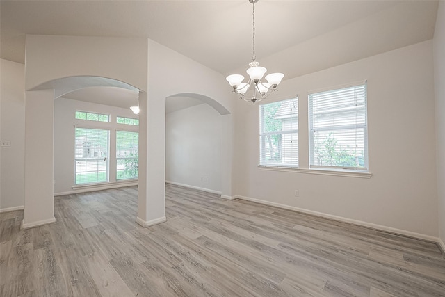 spare room with a chandelier, lofted ceiling, light wood-type flooring, and a healthy amount of sunlight