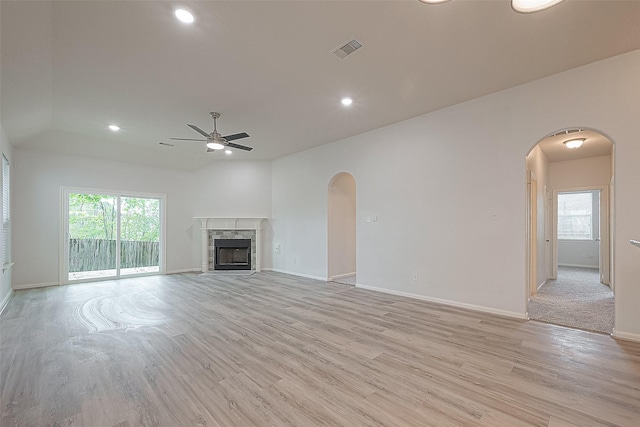 unfurnished living room featuring ceiling fan, a fireplace, light hardwood / wood-style floors, and lofted ceiling