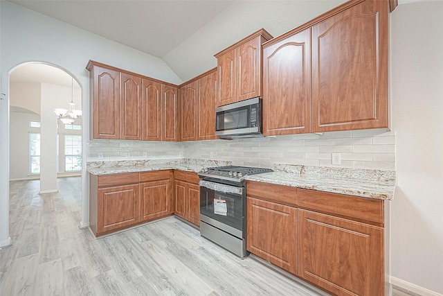 kitchen featuring appliances with stainless steel finishes, light wood-type flooring, backsplash, a notable chandelier, and lofted ceiling