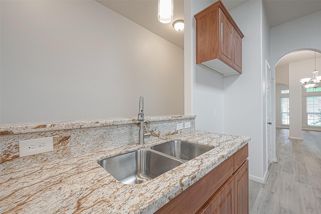 kitchen with sink, hanging light fixtures, light stone counters, a chandelier, and light hardwood / wood-style floors