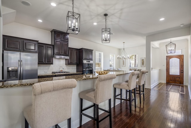 kitchen with a large island with sink, a breakfast bar, stainless steel appliances, and decorative light fixtures