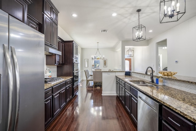 kitchen with pendant lighting, sink, dark brown cabinets, light stone counters, and stainless steel appliances