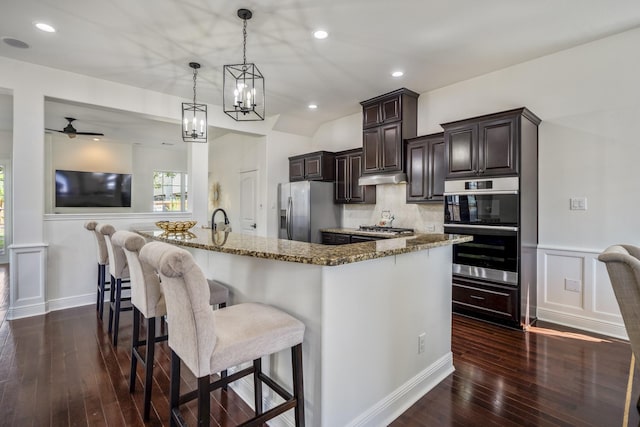 kitchen with a breakfast bar, ceiling fan with notable chandelier, hanging light fixtures, light stone counters, and stainless steel appliances