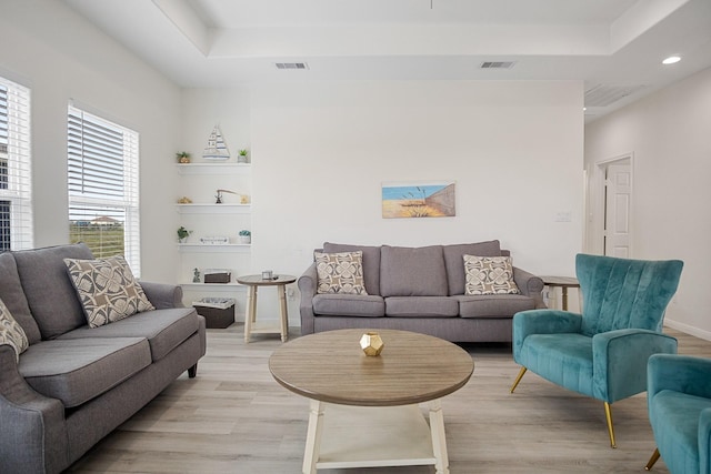 living room with light hardwood / wood-style floors and a tray ceiling