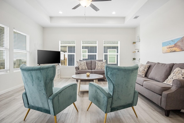 living room featuring ceiling fan, light hardwood / wood-style flooring, and a tray ceiling