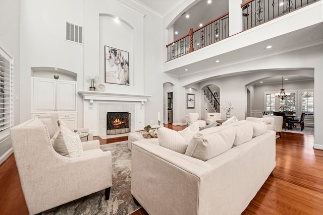 living room with a high ceiling, an inviting chandelier, hardwood / wood-style floors, a tiled fireplace, and ornamental molding