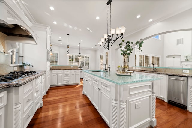 kitchen featuring white cabinets, hanging light fixtures, an island with sink, appliances with stainless steel finishes, and tasteful backsplash