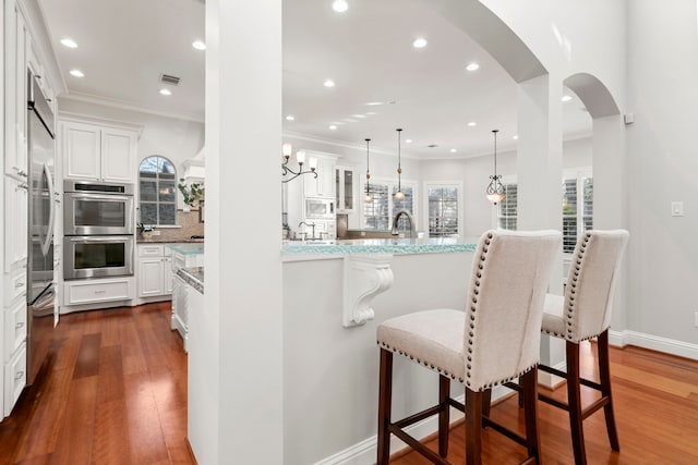 kitchen with white cabinets, a breakfast bar, double oven, and light stone countertops