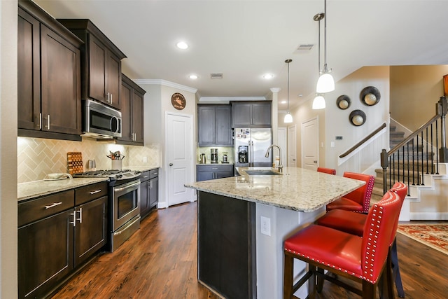 kitchen with a kitchen island with sink, sink, hanging light fixtures, appliances with stainless steel finishes, and dark hardwood / wood-style flooring