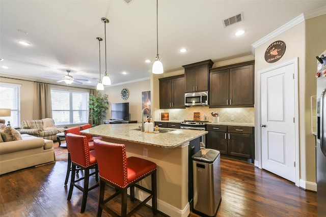 kitchen featuring a breakfast bar, a center island with sink, hanging light fixtures, light stone countertops, and stainless steel appliances