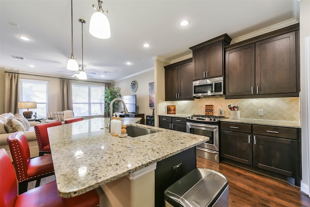 kitchen with sink, stainless steel appliances, an island with sink, decorative light fixtures, and a breakfast bar