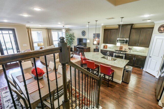 kitchen with a center island with sink, sink, light stone countertops, decorative light fixtures, and stainless steel appliances