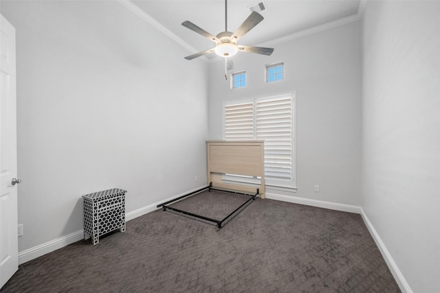 spare room with dark colored carpet, ceiling fan, ornamental molding, and a towering ceiling