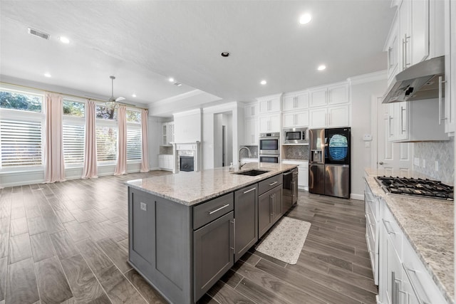 kitchen featuring decorative backsplash, white cabinets, stainless steel appliances, and an island with sink