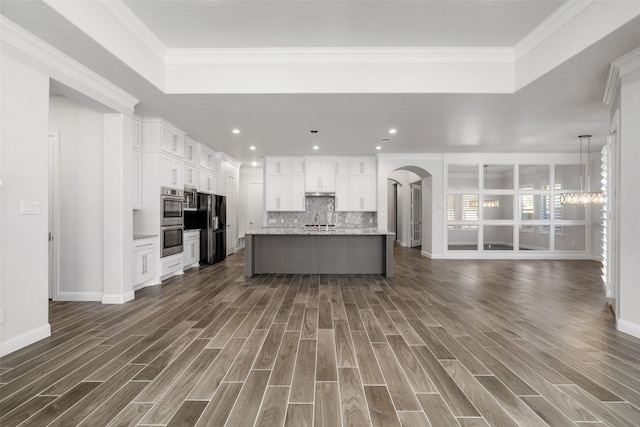 kitchen featuring black refrigerator, backsplash, ornamental molding, a center island with sink, and white cabinets