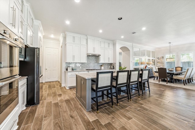 kitchen with light stone counters, crown molding, white cabinetry, and an island with sink