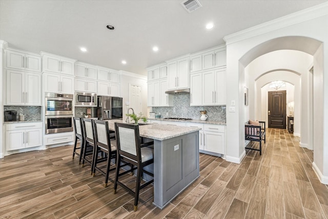 kitchen with an island with sink, light stone counters, white cabinetry, a breakfast bar area, and stainless steel appliances