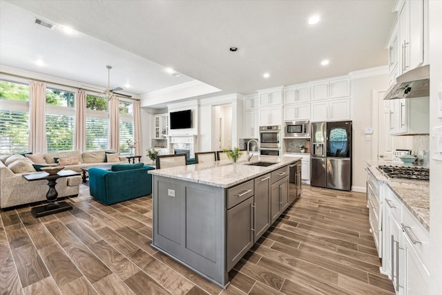 kitchen featuring a large island with sink, decorative backsplash, light stone counters, white cabinetry, and stainless steel appliances