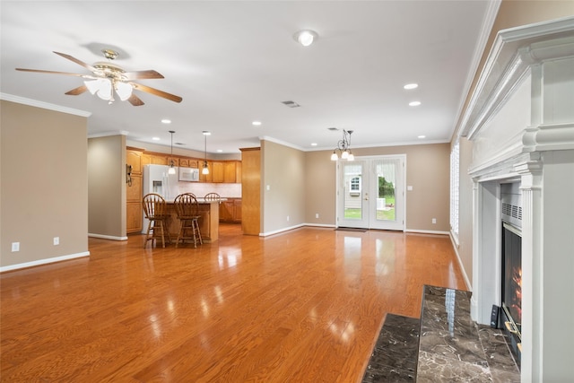 unfurnished living room featuring a high end fireplace, light wood-type flooring, ceiling fan with notable chandelier, and ornamental molding