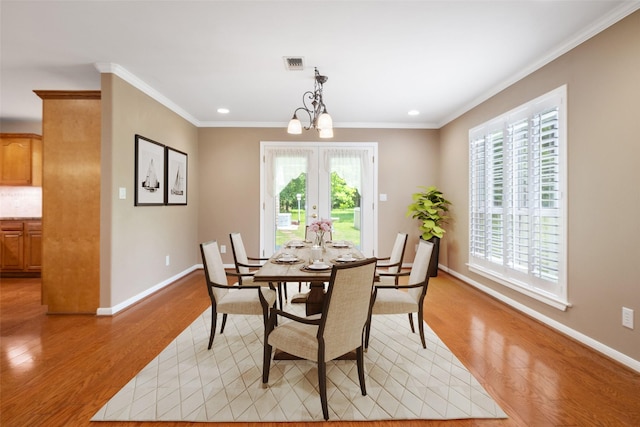 dining room with light wood-type flooring, ornamental molding, french doors, and a chandelier