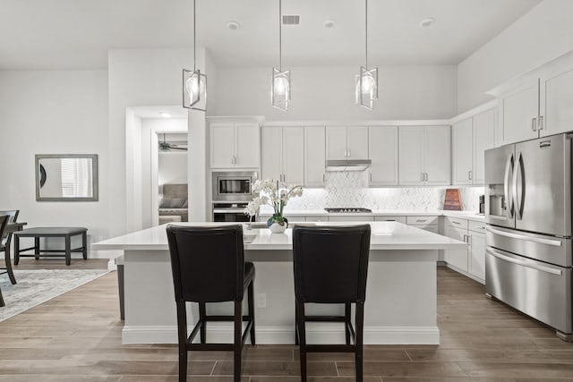 kitchen with white cabinets, stainless steel appliances, a kitchen island with sink, and a breakfast bar area