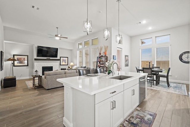 kitchen featuring white cabinetry, sink, hanging light fixtures, stainless steel dishwasher, and a kitchen island with sink