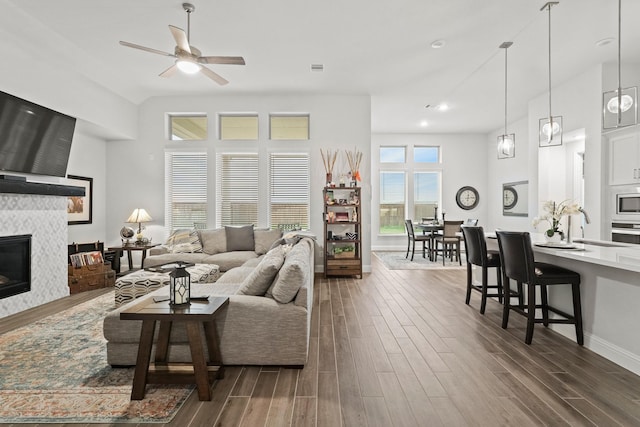 living room featuring a tile fireplace, ceiling fan, and dark wood-type flooring