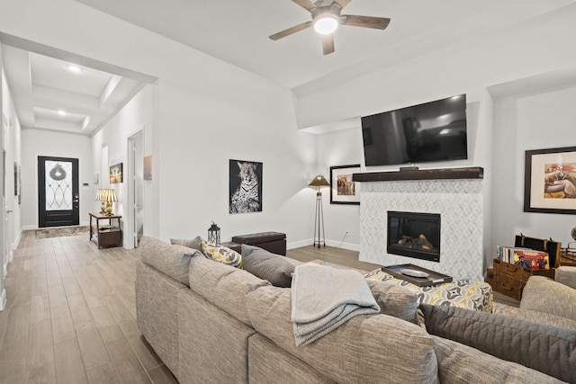 living room with a fireplace, light wood-type flooring, a raised ceiling, and ceiling fan