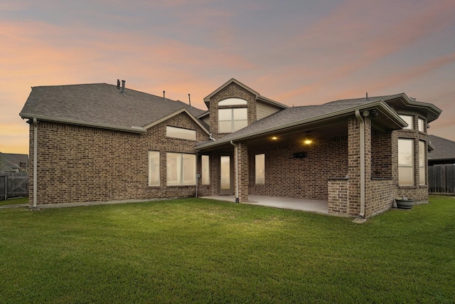 back house at dusk featuring a patio area and a yard