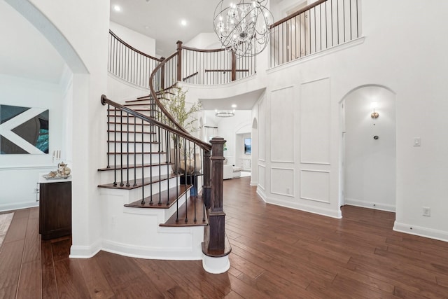 stairway featuring a chandelier, a towering ceiling, and wood-type flooring