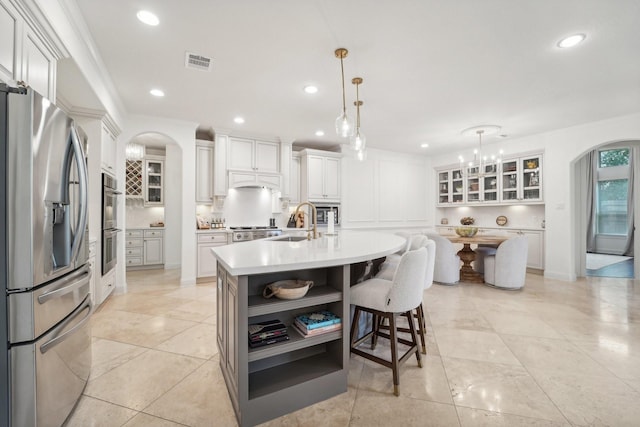 kitchen featuring appliances with stainless steel finishes, sink, decorative light fixtures, white cabinetry, and an island with sink