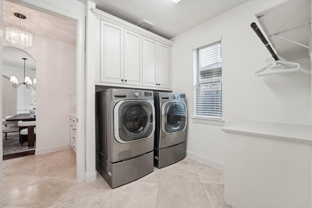 clothes washing area with cabinets, an inviting chandelier, washer and clothes dryer, and light tile patterned flooring