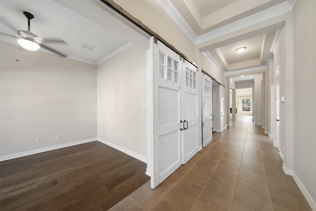 hall featuring a barn door, a tray ceiling, dark hardwood / wood-style floors, and crown molding