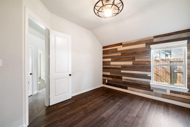 empty room featuring dark hardwood / wood-style flooring, lofted ceiling, and wood walls