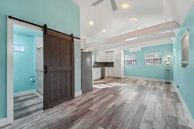 kitchen featuring a barn door, light hardwood / wood-style floors, decorative backsplash, stainless steel appliances, and white cabinets