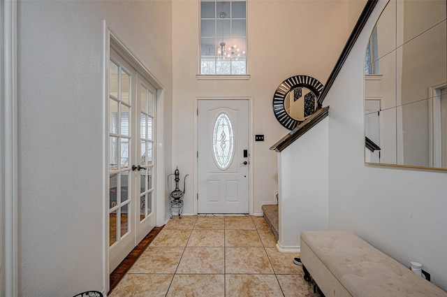 tiled foyer entrance with a high ceiling, an inviting chandelier, and french doors