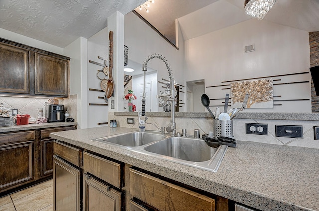 kitchen with vaulted ceiling, sink, backsplash, light tile patterned floors, and dark brown cabinetry