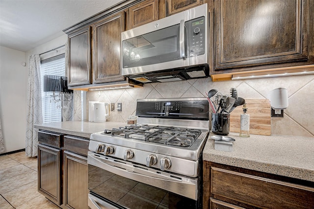 kitchen with light tile patterned floors, dark brown cabinets, stainless steel appliances, light stone countertops, and decorative backsplash