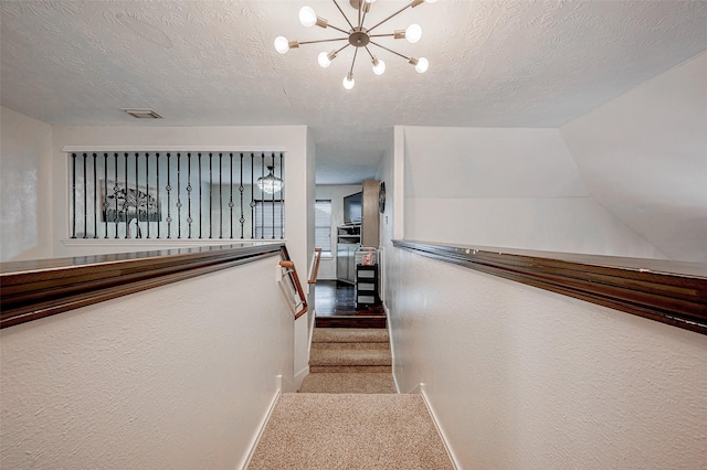 staircase featuring carpet flooring, a textured ceiling, and a notable chandelier