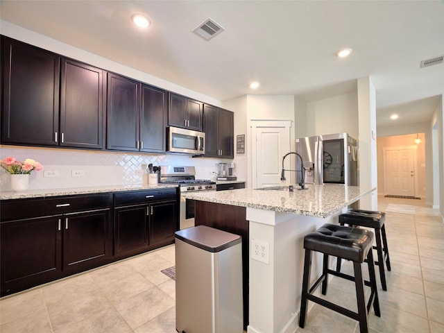 kitchen with sink, a breakfast bar area, decorative backsplash, a center island with sink, and appliances with stainless steel finishes