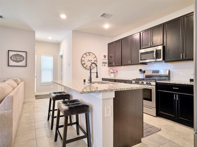 kitchen featuring stainless steel appliances, sink, light tile patterned floors, a breakfast bar area, and an island with sink