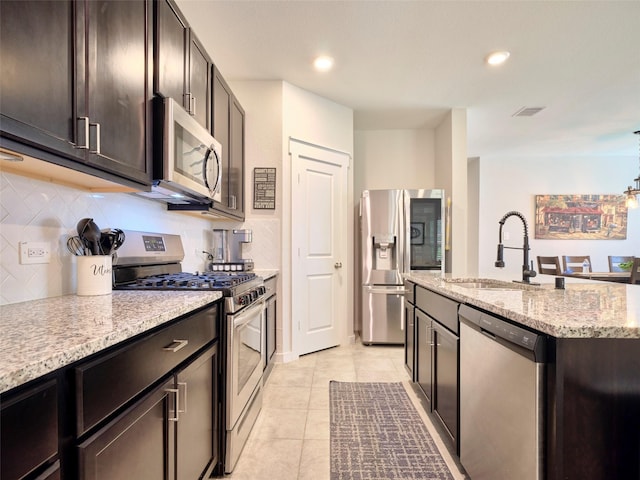 kitchen featuring sink, light tile patterned floors, an island with sink, appliances with stainless steel finishes, and light stone counters