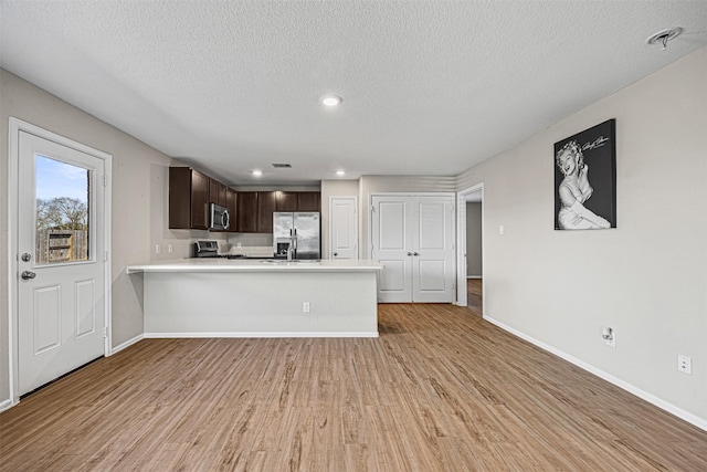 kitchen featuring a textured ceiling, dark brown cabinetry, appliances with stainless steel finishes, kitchen peninsula, and light hardwood / wood-style flooring