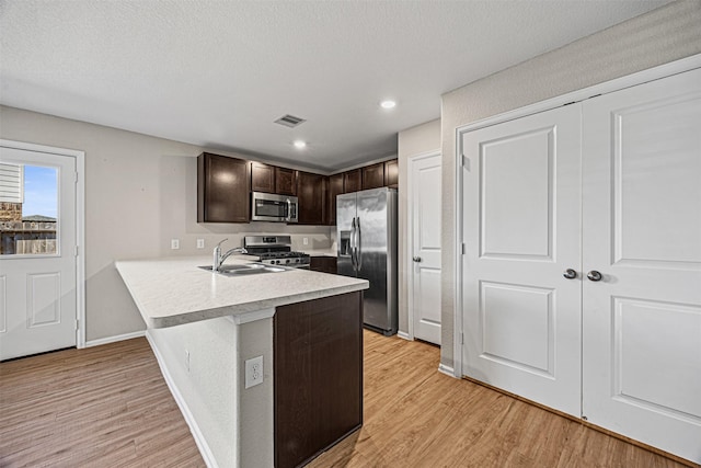 kitchen with kitchen peninsula, appliances with stainless steel finishes, sink, light wood-type flooring, and dark brown cabinetry