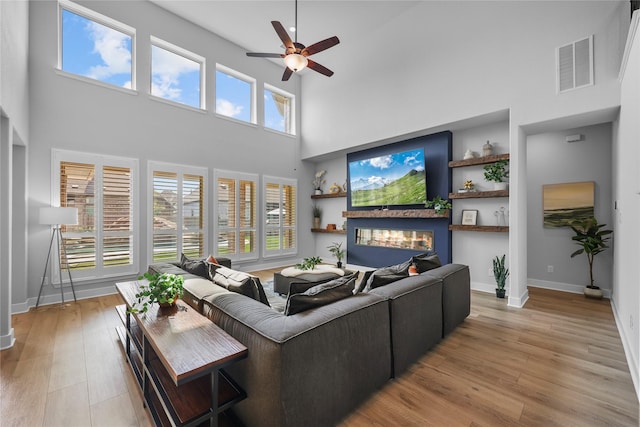 living room featuring ceiling fan, built in shelves, a high ceiling, and light hardwood / wood-style flooring