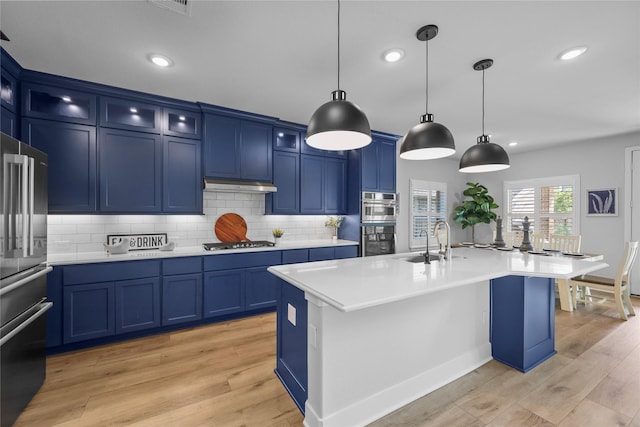 kitchen with blue cabinetry, decorative light fixtures, a kitchen island with sink, and sink