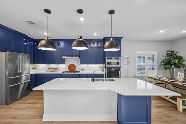 kitchen featuring sink, blue cabinets, stainless steel appliances, and an island with sink