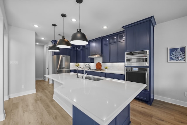 kitchen with appliances with stainless steel finishes, light wood-type flooring, blue cabinets, sink, and a center island with sink